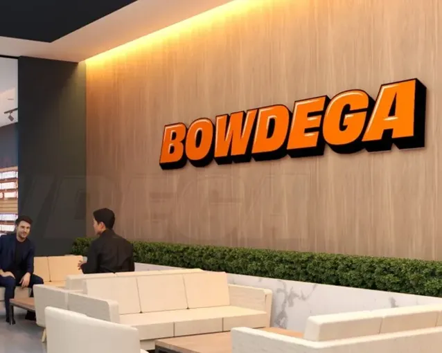 Modern lounge area with two men talking and a large orange 'BOWDEGA' sign on a wooden wall Modern lounge area with two men talking and a large orange 'BOWDEGA' sign on a wooden wall.