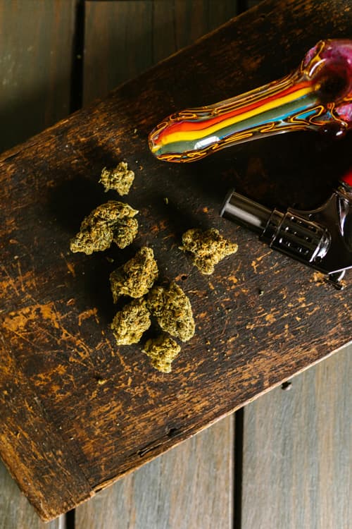 Glass pipe and cannabis buds Glass pipe and cannabis buds displayed on a rustic wooden surface.